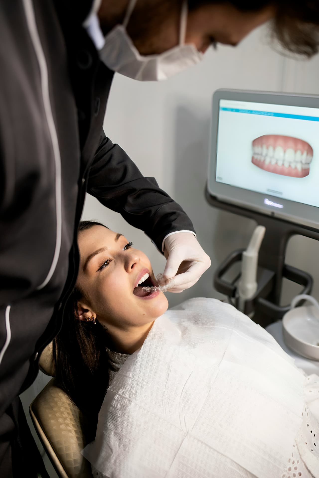 Dental professional fitting a clear aligner for a patient beside a 3D digital scan of her teeth