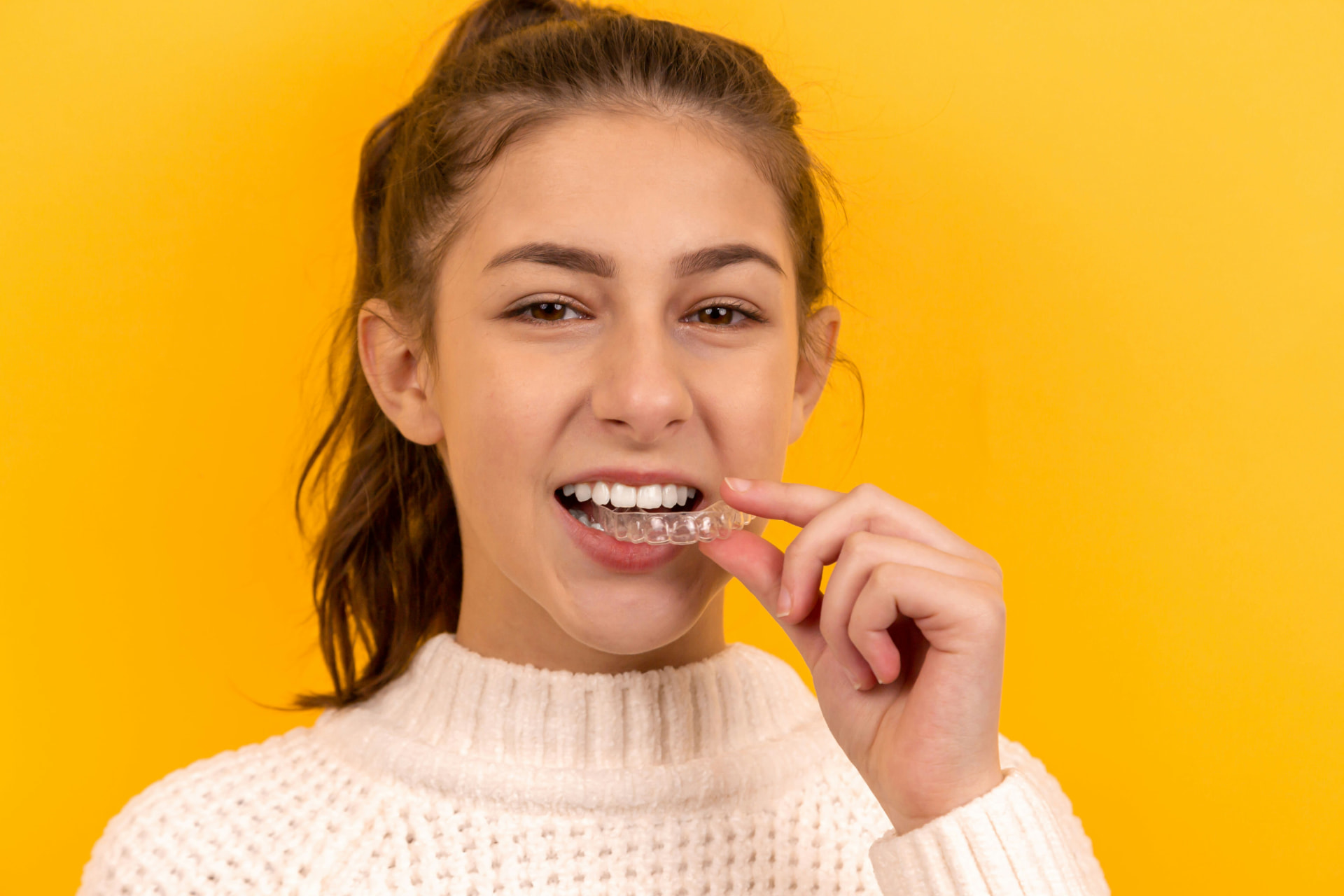 Young woman placing a clear aligner tray over her upper teeth