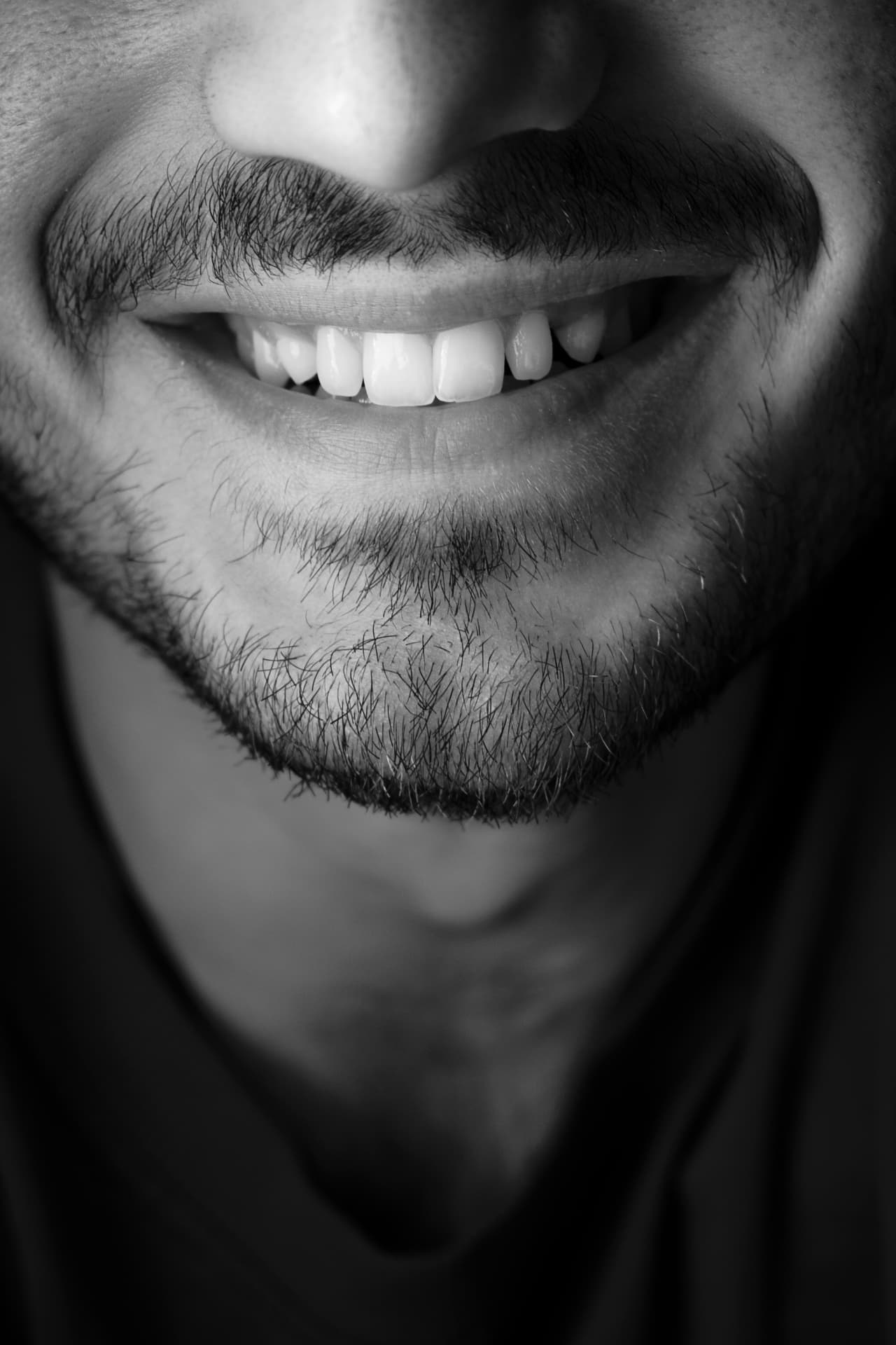 Black-and-white close-up of a bearded man's smile with bright, well-shaped teeth