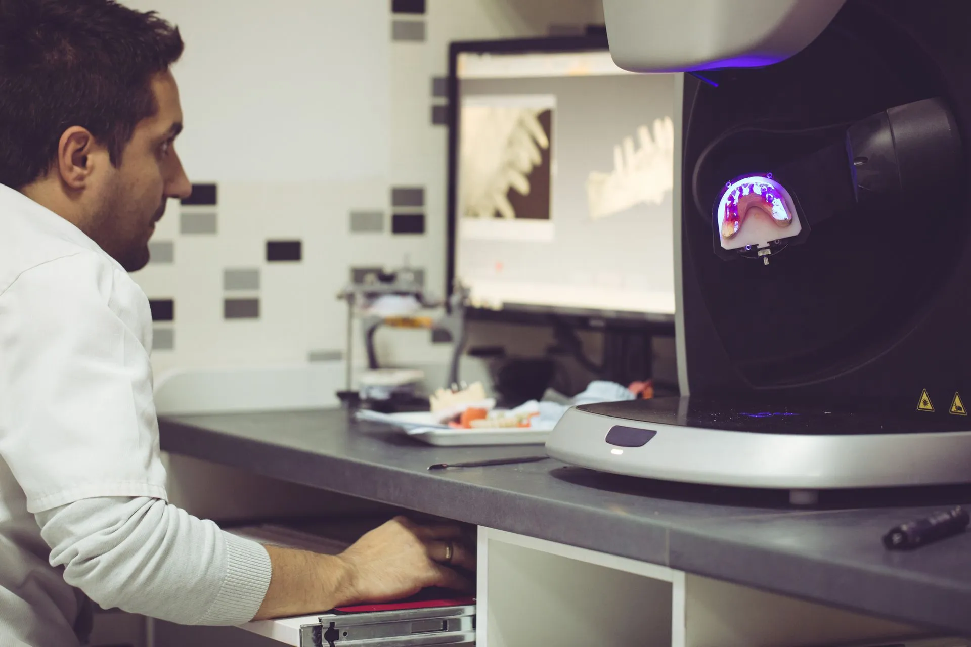 Dental technician designing a restoration on CAD software beside a lab scanner